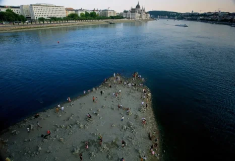 Personas caminan sobre un banco de arena bajo el puente Margareth del Danubio en el centro de Budapest, Hungría, el miércoles 5 de agosto de 2026, mientras el río ha retrocedido a niveles de agua nunca antes vistos.