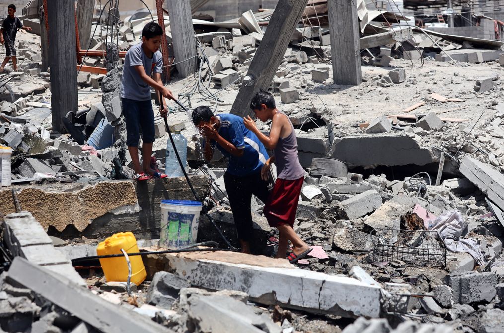 Niños palestinos se refrescan y llenan jarras de agua en el campo de refugiados de Nuseirat, en el centro de Gaza, en medio de una ola de calor el 9 de junio, un día después de una operación mortal de las fuerzas israelíes para rescatar rehenes. Crédito: Majdi Fathi/NurPhoto/Getty Images