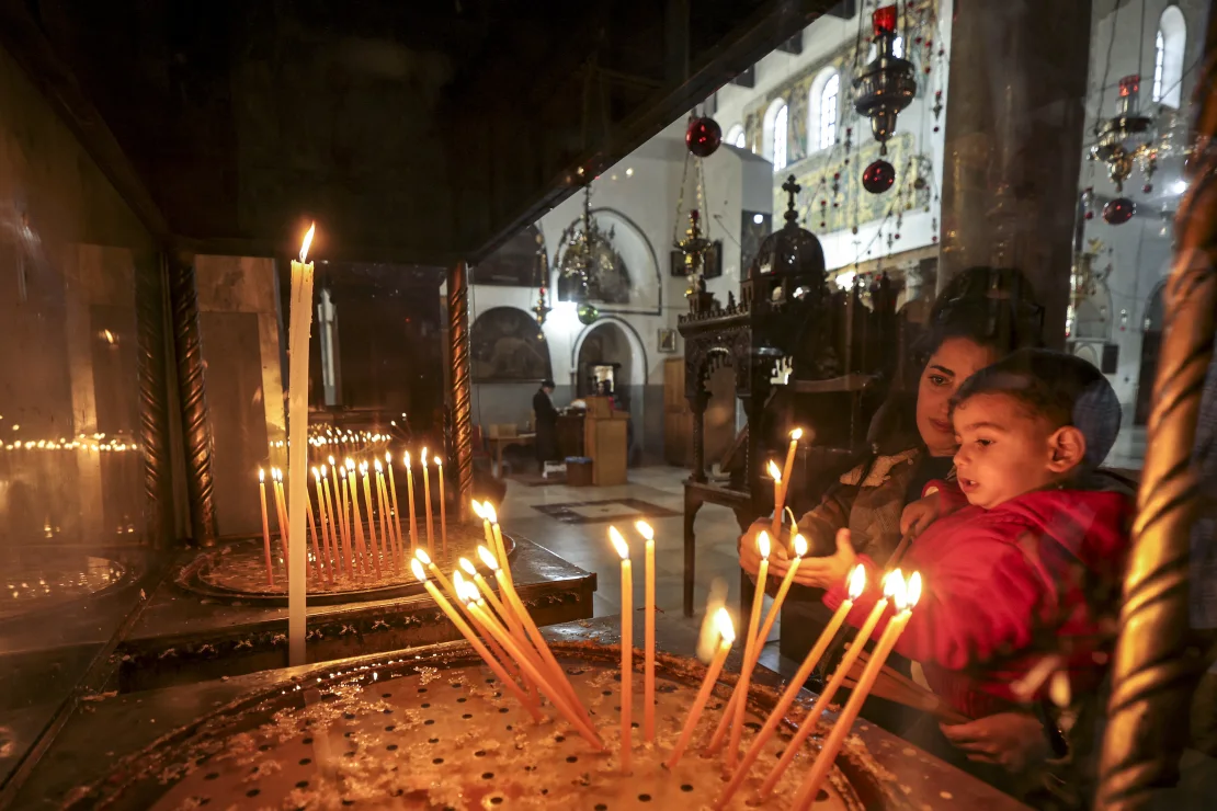 Una mujer y un niño encienden velas en la Basílica Griega del Complejo de la Iglesia de la Natividad en Belén, en la Cisjordania ocupada, el 22 de diciembre de 2024. HAZEM BADER/AFP/AFP vía Getty Images