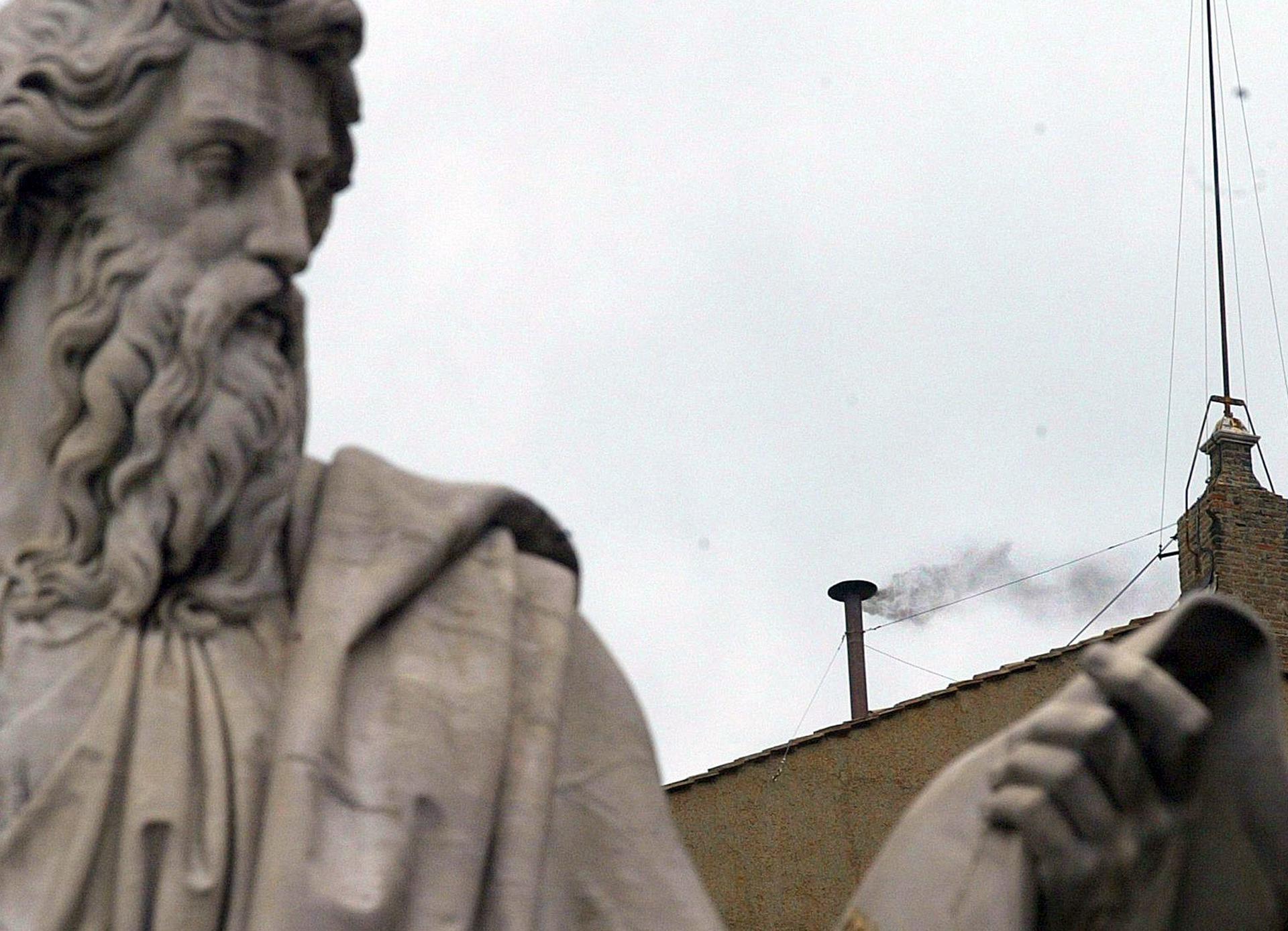 Imagen de archivo del humo negro que sale de la chimenea del tejado de la Capilla Sixtina tras una de las estatuas de la Plaza de San Pedro del Vaticano. EFE/Danilo Schiavella