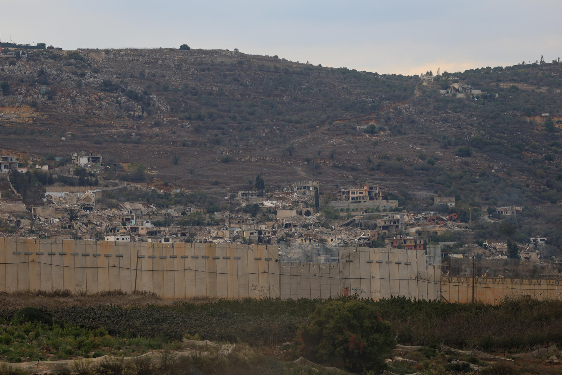El alto el fuego entre Israel y el Líbano cumple este jueves un año marcado por los bombardeos diarios del Ejército israelí en territorio libanés. Este domingo, a tan sólo cuatro días de que la tregua cumpliera el año, culminaron con un ataque contra los suburbios de Beirut que mató al líder militar del grupo chií Hizbulá, Haizam Ali Tabatabai. Frontera entre el Líbano e Israel, tomada desde la localidad israelí de Metula. Muro que muestra la división entre los dos países, y la destrucción de las viviendas del lado libanés. EFE/Magda Gibelli