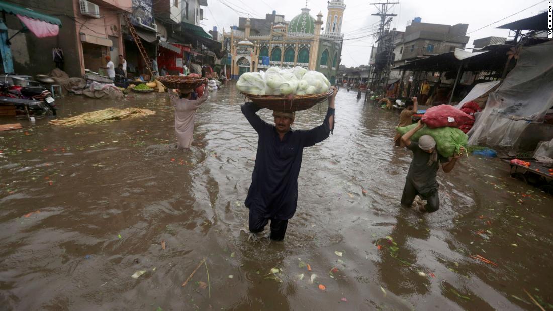 Los trabajadores cargan productos mientras caminan por un camino inundado después de fuertes lluvias, en Lahore, Pakistán, el jueves 21 de julio de 2022.